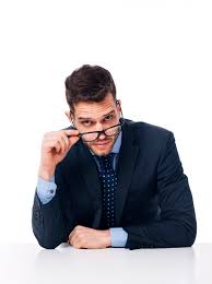 Confused man in dark blue suit holding glasses off his nose.